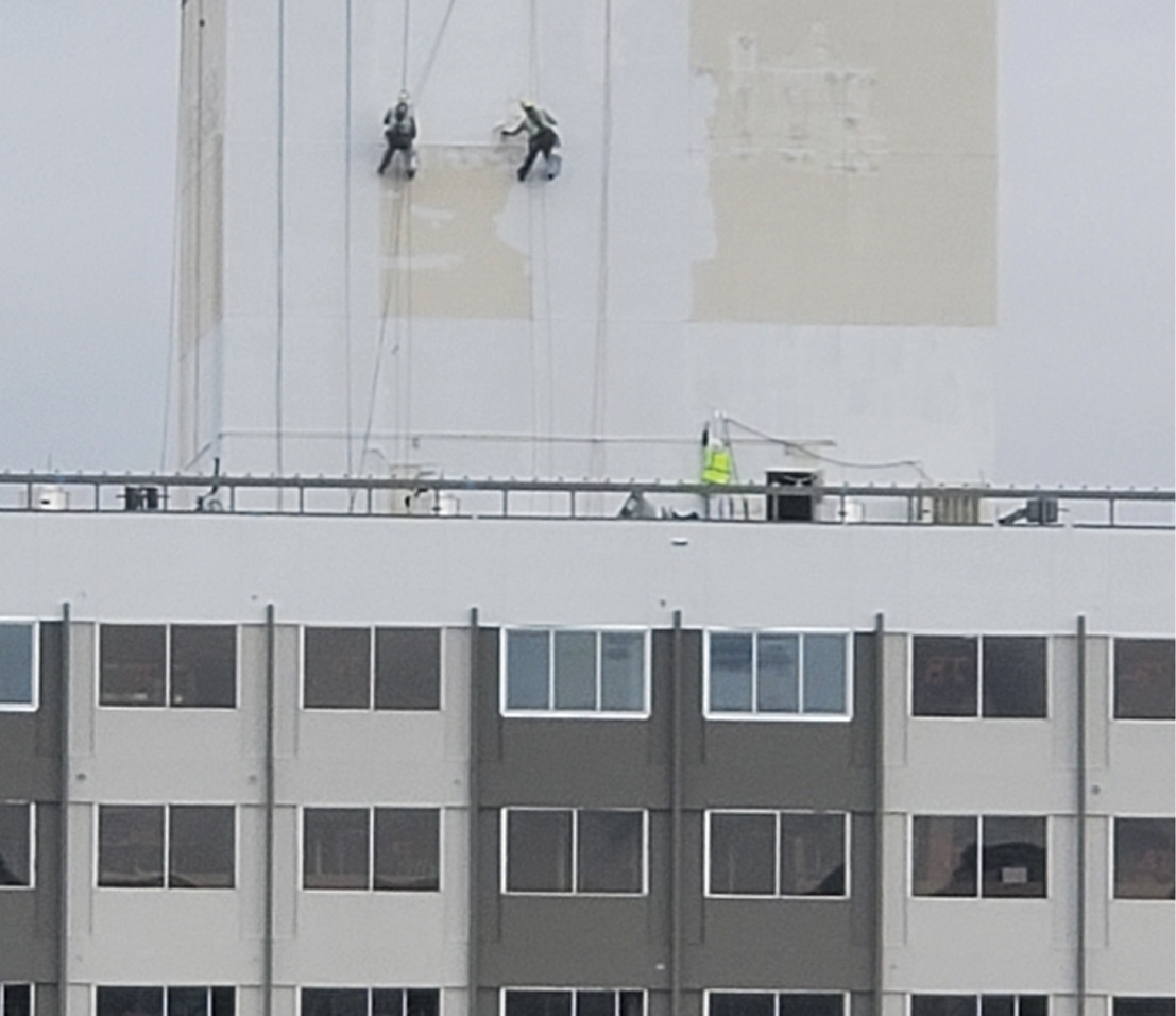 Workers painting a tall building façade.