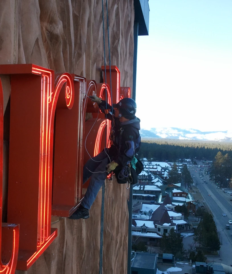Person climbing and repairing large neon sign.